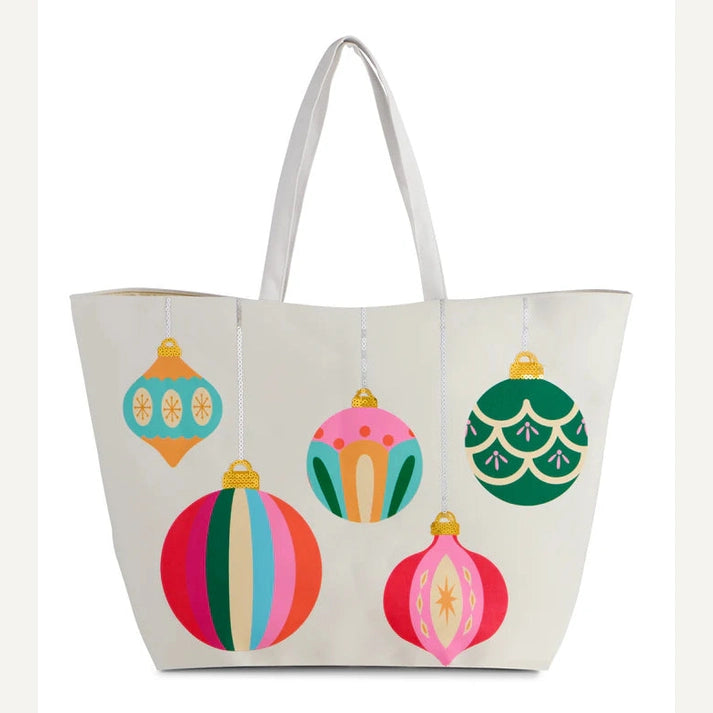 Canvas tote bag by Draper James featuring five vibrant holiday ornaments with gold sequined caps including a multi-colored striped bauble and a pink starburst teardrop ornament against a white background