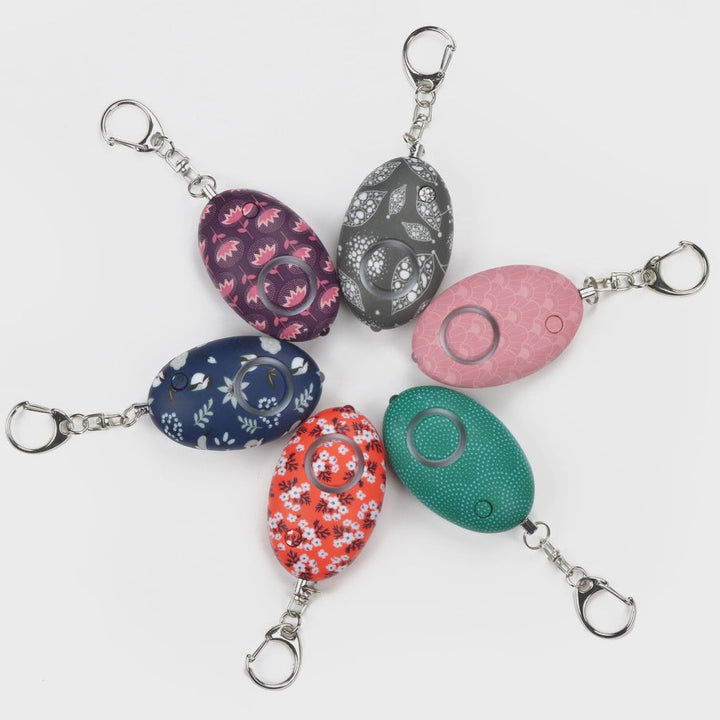 Six egg-shaped alarm keychains in floral, teal, pink and gray patterns arranged in a circle