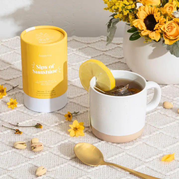 Yellow Sips of Sunshine tea canister beside a mug of tea with a lemon slice and yellow flowers
