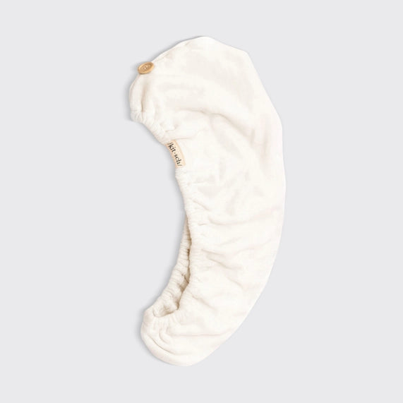 Product photography by Kitsch of a white microfiber hair towel wrap featuring a small wooden button, a branded beige tag, and a gathered elastic edge on a neutral studio background