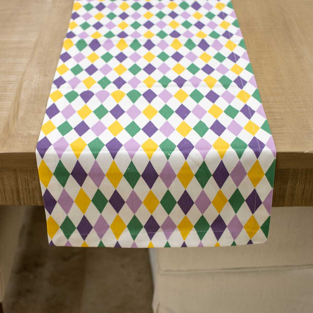 Table runner with purple, green and gold harlequin diamonds draped over a wooden table