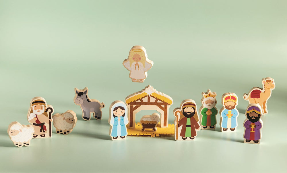 Painted wooden nativity figures with a stable, angel, shepherd, wise men, sheep, donkey and camel on a green surface