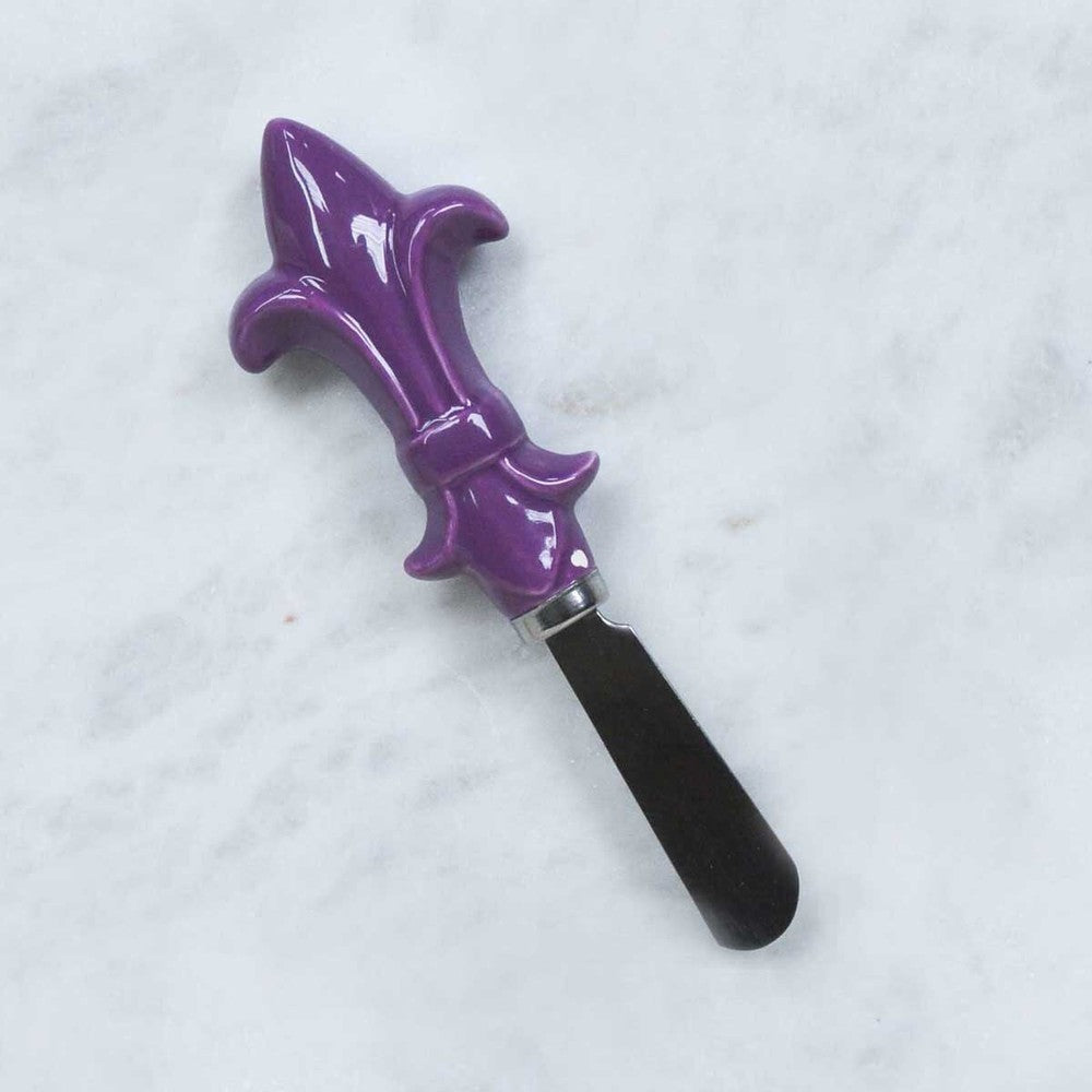 Spreader with a purple ceramic fleur-de-lis handle on a marble surface
