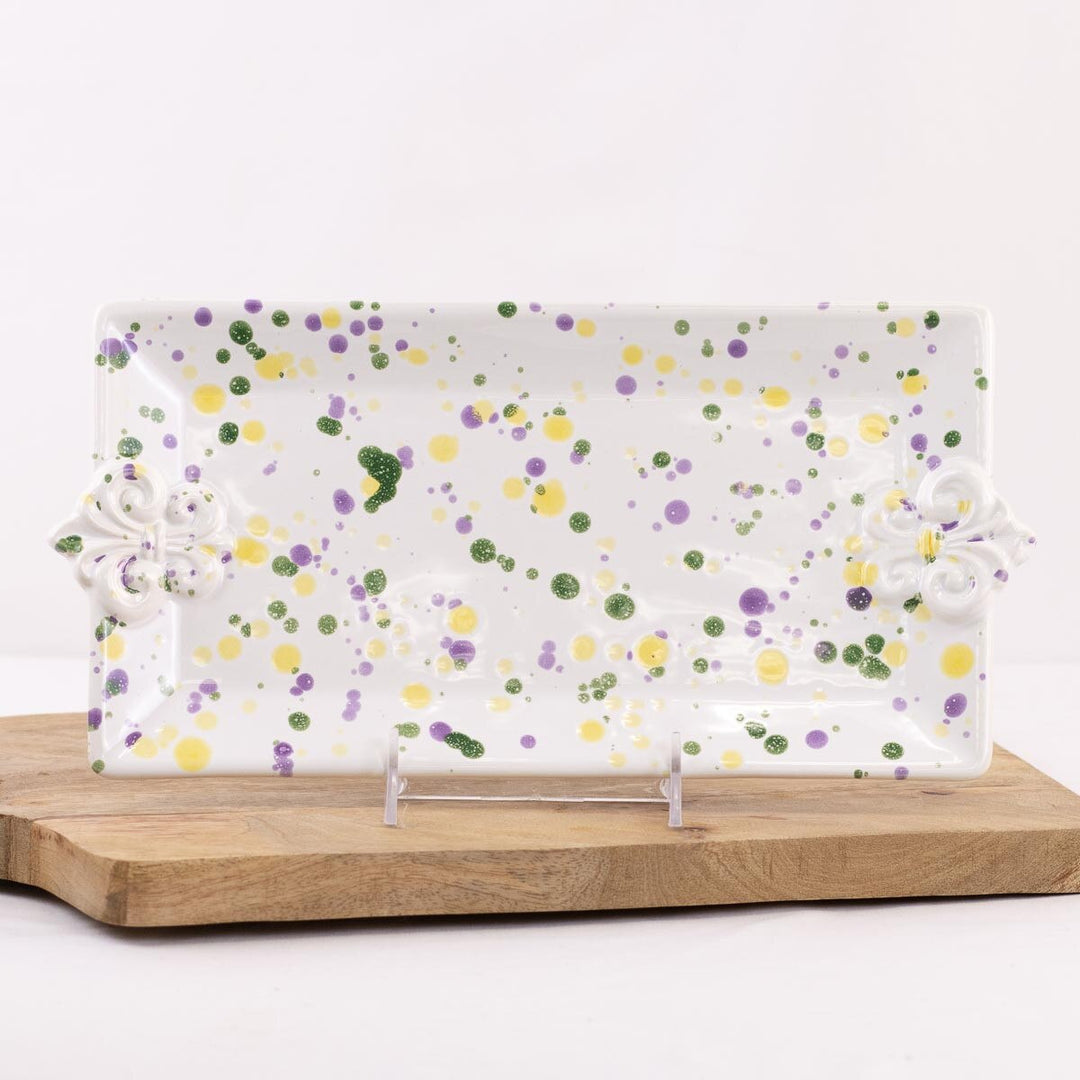 White rectangular platter with fleur de lis handles and purple, green and yellow splatter, displayed on a stand