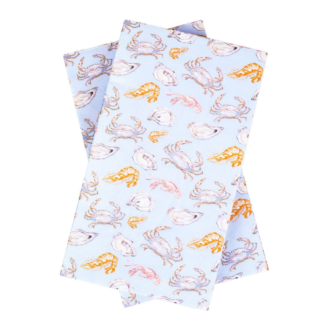 Watercolor printed napkins featuring a repeating coastal pattern of detailed blue crabs, vibrant orange shrimp, and oyster shells against a soft periwinkle background on a white surface