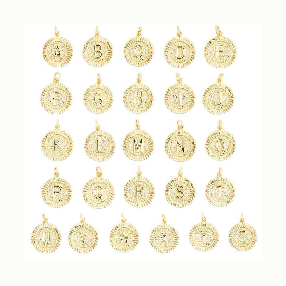 Gold jewelry pendants featuring a collection of twenty-six alphabet initial charms from A to Z displayed against a white background with decorative fluted sunray borders, hammered metal textures, and polished raised lettering
