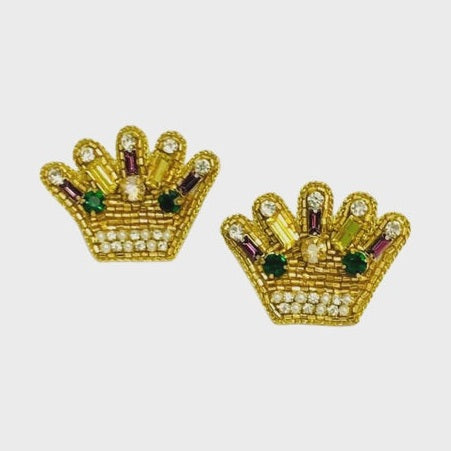 Hand-beaded crown earrings crafted with metallic gold seed beads and vibrant emerald green and amethyst purple crystals against a minimalist white background