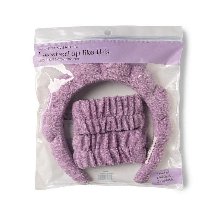 Studio product photograph by Lemon Lavender of a three-piece spa set in a clear bag, featuring a soft lavender plush bubble-style headband and matching ruched wristbands with the i washed up like this slogan visible