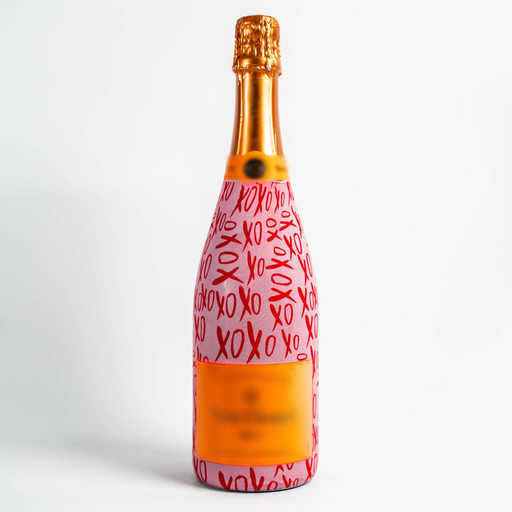 Champagne bottle with orange label wearing a pink wrap printed with red XOXO