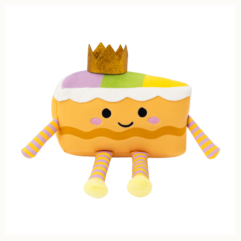 Plush toy of a festive Mardi Gras King Cake character featuring a glittering gold crown, purple and yellow striped limbs, and white scalloped icing isolated on a white background