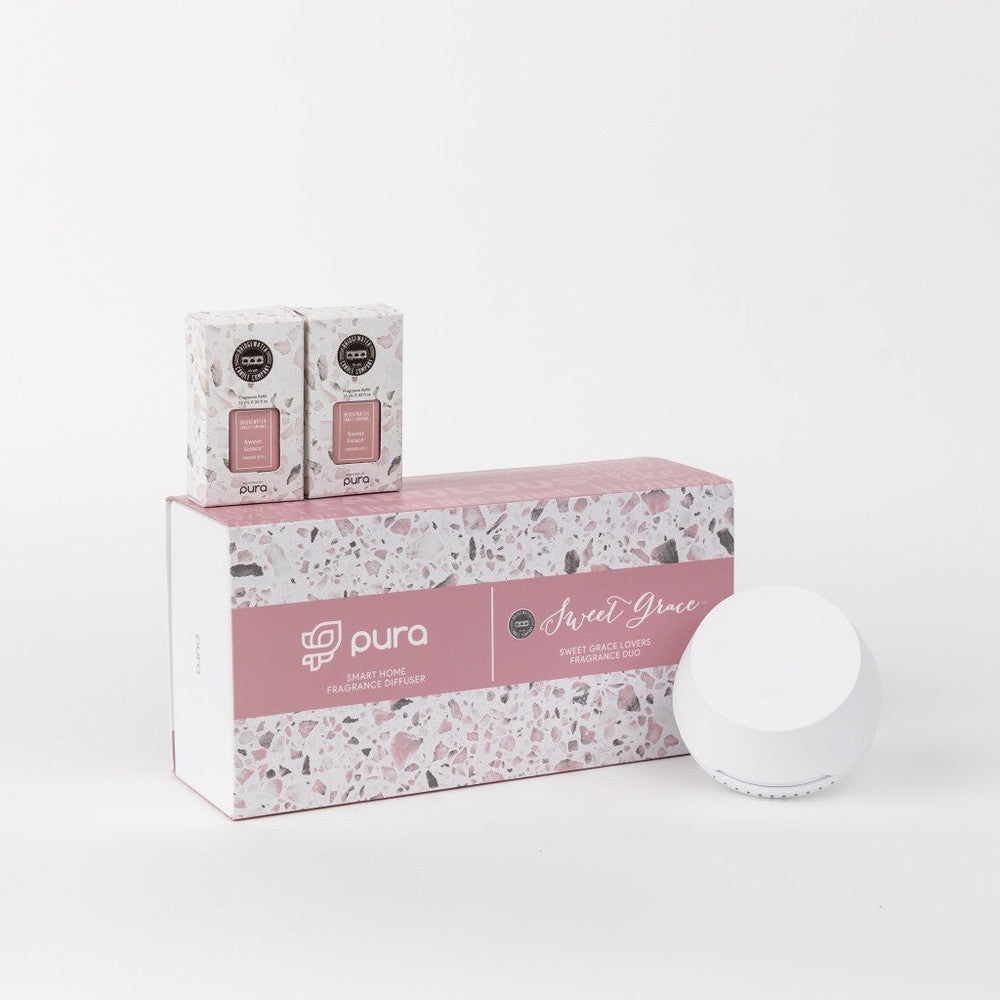 Product photography by Pura of the Sweet Grace Lovers Fragrance Duo kit on a white background showcasing a large box with a pink and gray terrazzo design, two individual Bridgewater Candle Company refills, and a sleek white circular smart home fragrance diffuser