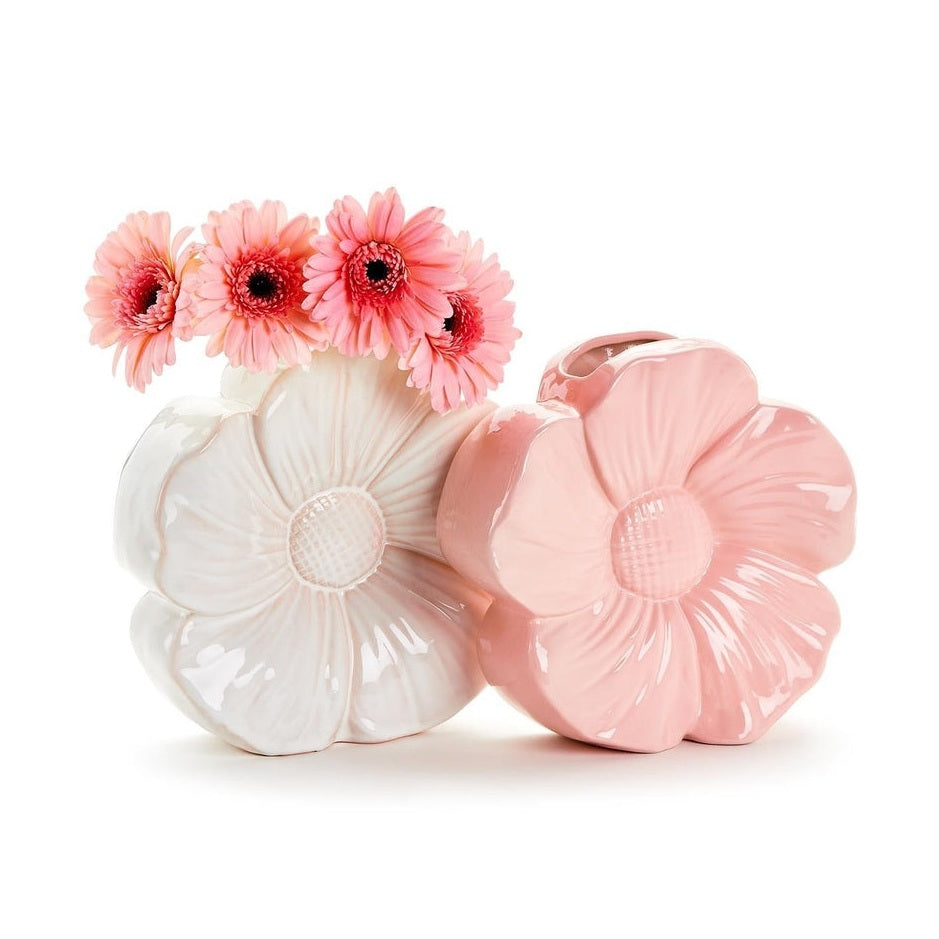 Glazed ceramic flower-shaped vases in white and pink displayed on a neutral surface featuring a high-gloss finish, intricate relief petal textures, and a cluster of vibrant pink gerbera daisies blooming from the white vessel