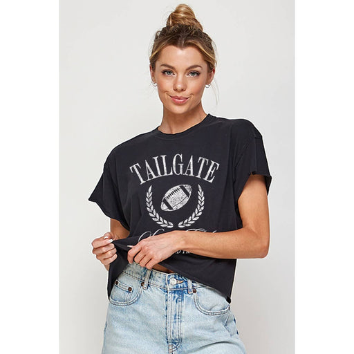 Studio fashion photography of a woman in a white studio wearing a black graphic t-shirt with a distressed white Tailgate football print and light-wash denim jeans with her hair in a sleek high bun