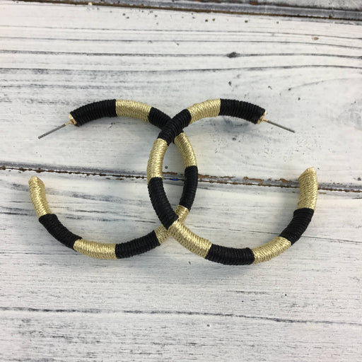 Handmade thread-wrapped jewelry featuring large interlocking hoop earrings with a black and metallic gold striped pattern displayed on a white distressed wood background
