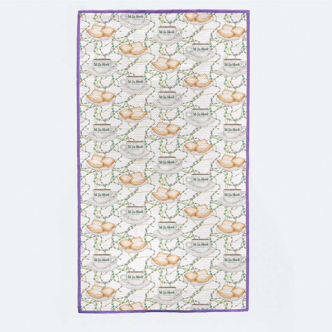 Kitchen towel printed with beignets, coffee cups and Mardi Gras beads, with purple trim