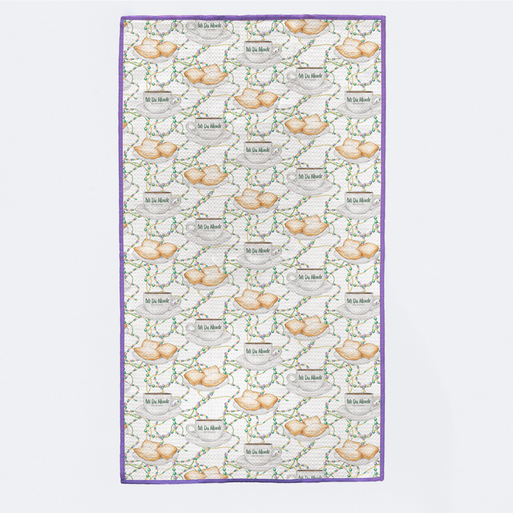 Kitchen towel printed with beignets, coffee cups and Mardi Gras beads, with purple trim