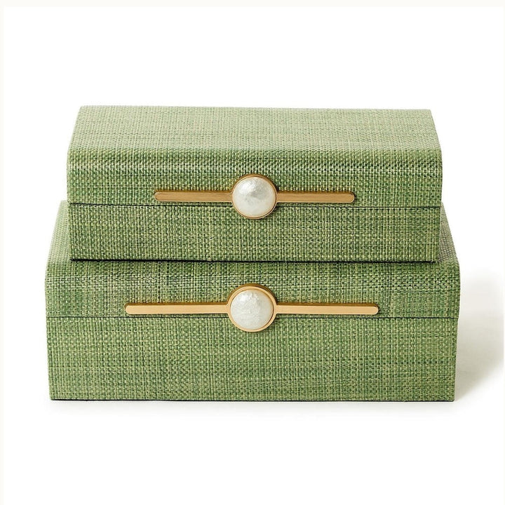 Grasscloth and gold-finished metal decorative boxes stacked on a white background showcasing a sage green basketweave texture, elongated horizontal gold-tone hardware, and iridescent white marble-like central accents