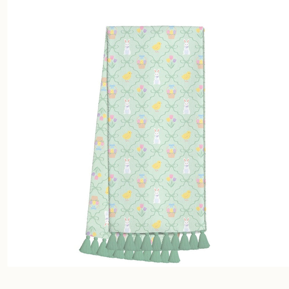 Textile hand towel featuring an Easter-themed trellis pattern on a mint green background with motifs of white rabbits wearing purple bowties, fluffy yellow chicks, and colorful tulips finished with a row of sage green tassels against a plain white backdrop