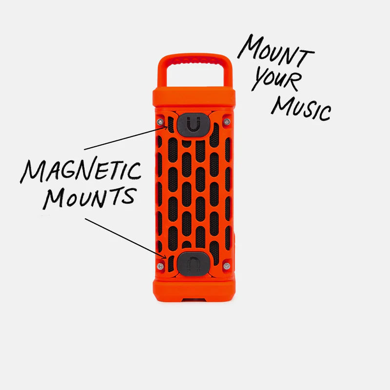 Product photograph of a bright orange rugged portable speaker featuring a black honeycomb grille and two integrated magnetic mounts with handwritten text overlays on a minimalist white background