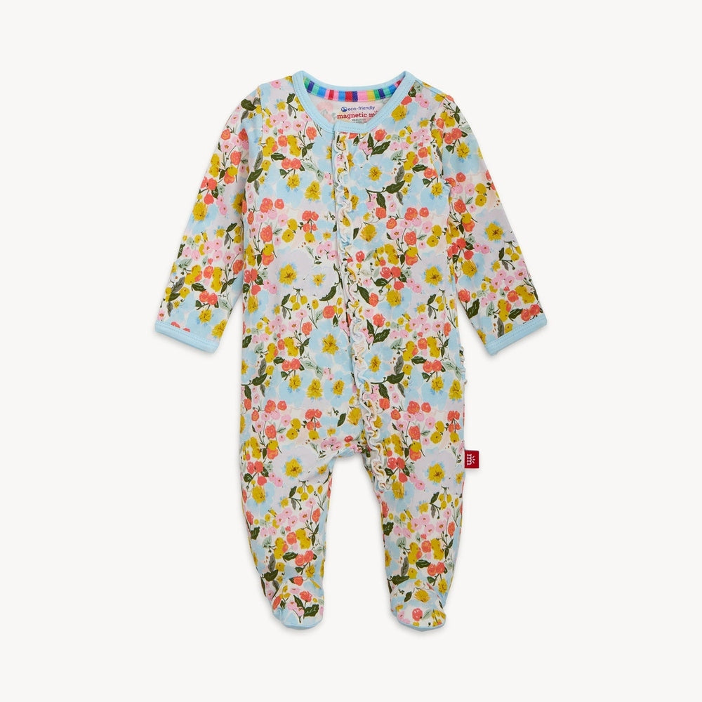 Product photograph of a Magnetic Me baby footie onesie on a white background featuring a vibrant pink and yellow floral print with a delicate ruffle along the front magnetic closure and light blue trim at the collar and cuffs