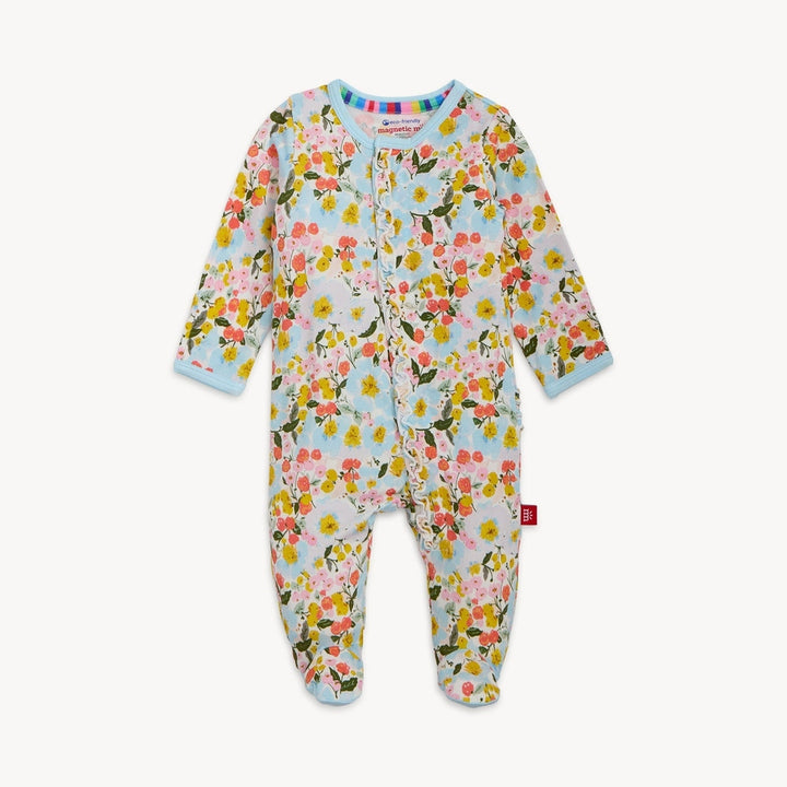 Product photograph of a Magnetic Me baby footie onesie on a white background featuring a vibrant pink and yellow floral print with a delicate ruffle along the front magnetic closure and light blue trim at the collar and cuffs