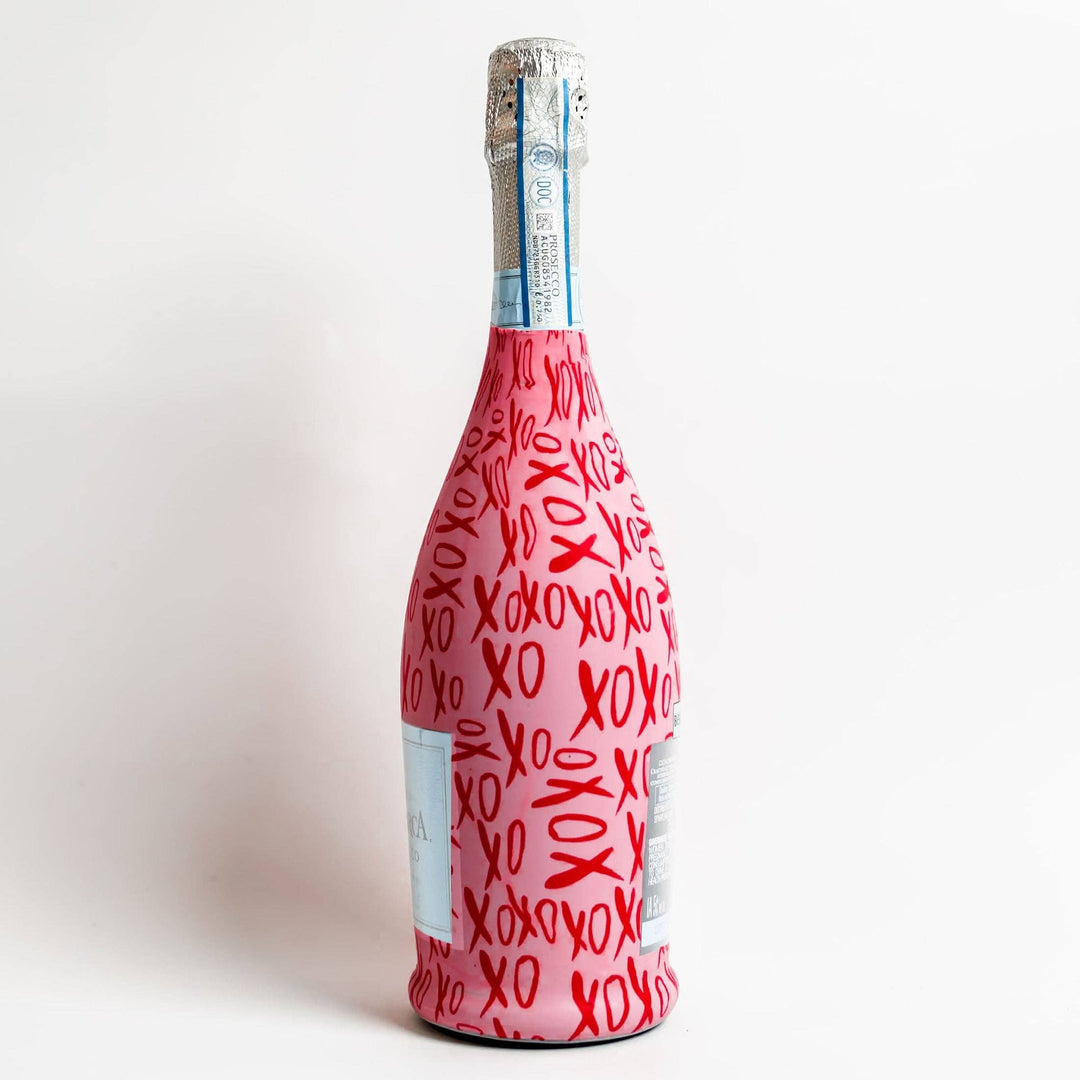Side view of a prosecco bottle in a pink and red XOXO print wrap