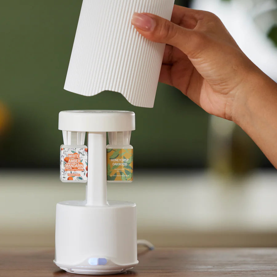 Hand lifting the ribbed cover off a white diffuser, showing two fragrance vials inside