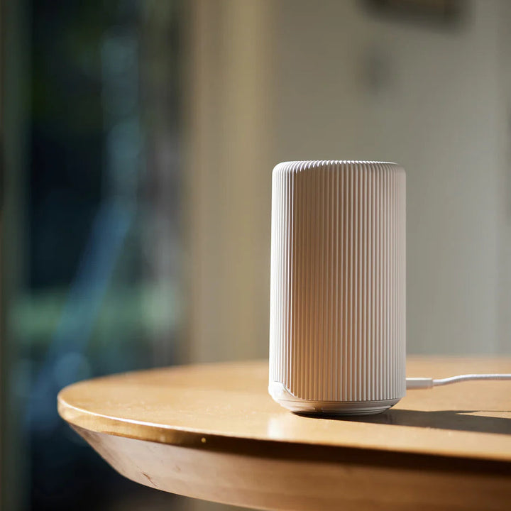 White ribbed cylindrical diffuser on a round wooden table