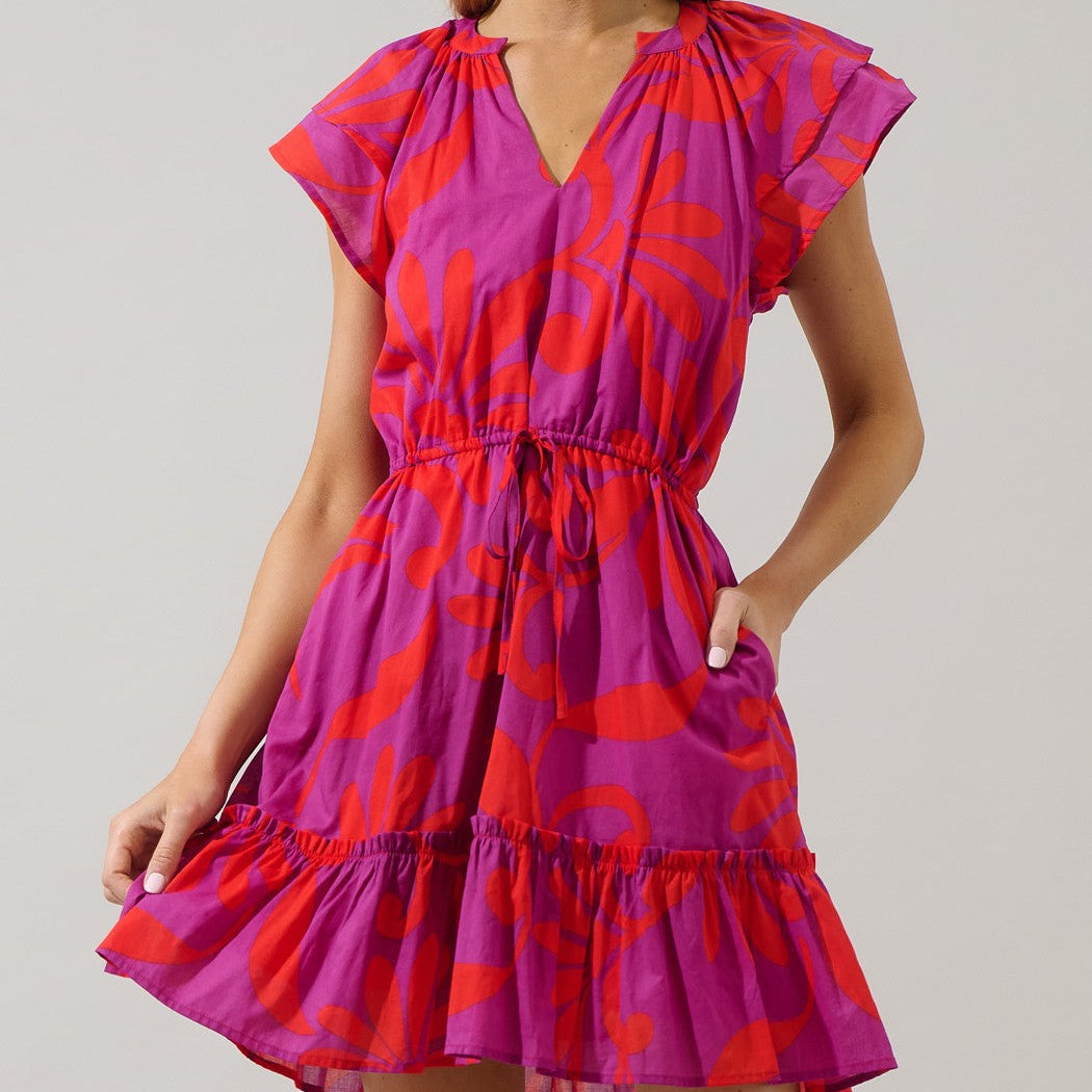 Digital studio photograph of a model wearing a short magenta and orange abstract floral print dress featuring tiered flutter sleeves, a cinched drawstring waist, and a ruffled hem