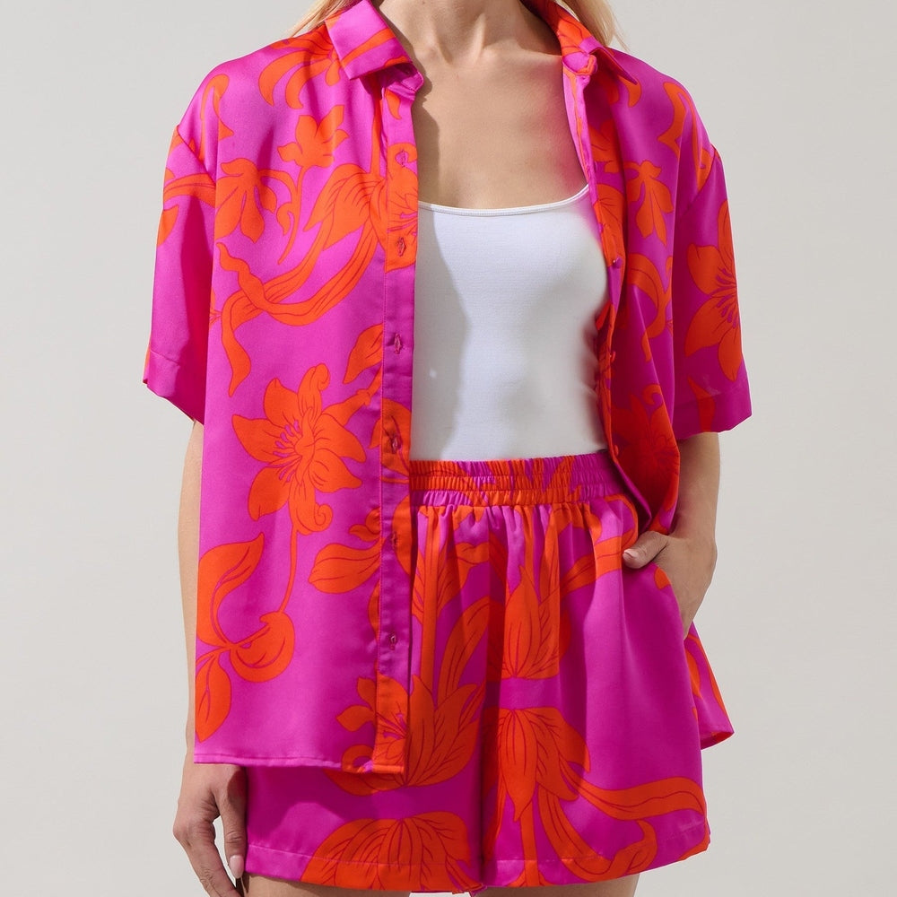 Photograph of a woman modeling a vibrant fuchsia pink and bright orange floral print satin-like matching set including a short-sleeved button-down shirt and elastic-waist shorts in a clean studio environment