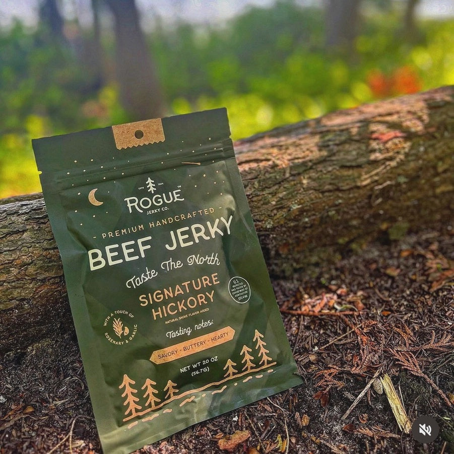 Rogue Signature Hickory beef jerky bag leaning against a mossy log outdoors
