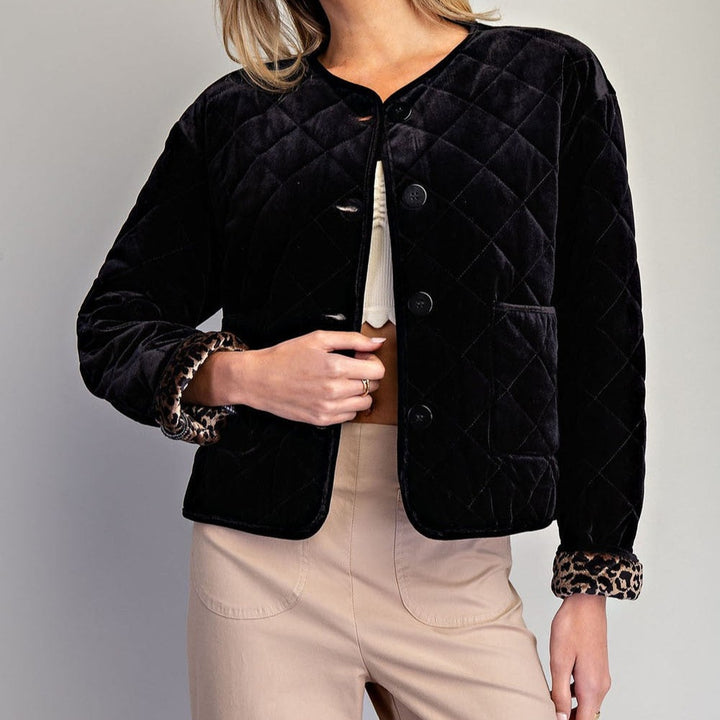 Woman wearing a black quilted velvet button-front jacket with leopard-print cuffs and tan trousers