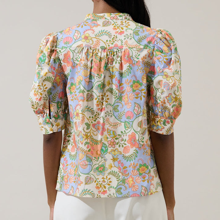 Photograph of a floral Hermès blouse worn by a model in a studio featuring an intricate botanical print with pastel orange flowers, light blue patterns, and pleated puff sleeves