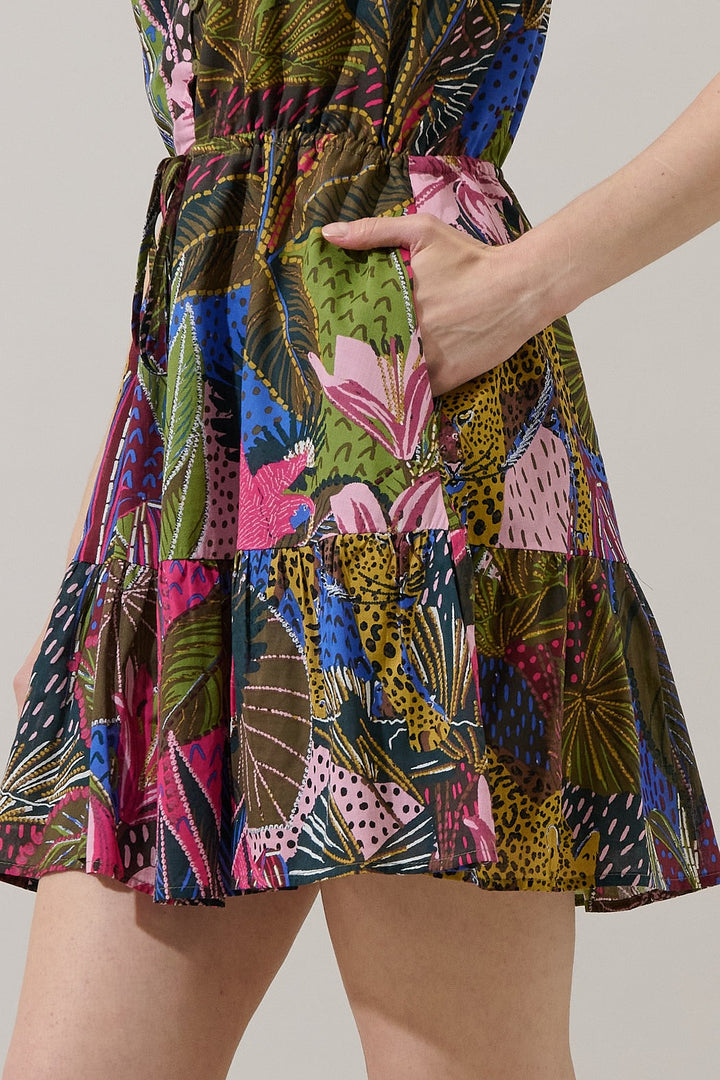 Photograph of a vibrant Farm Rio mini dress featuring a colorful tropical jungle print with large pink lilies, spotted leopard motifs, and lush green palm leaves in a studio setting