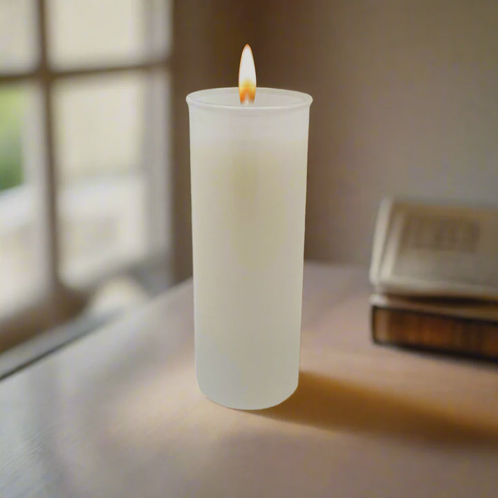 Lit white votive candle in frosted glass on a table near a window