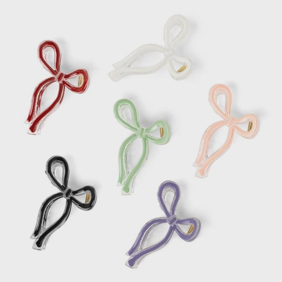 Studio photograph of six bow-shaped resin hair claw clips in cherry red, mint green, and lavender hues scattered on a neutral background featuring translucent edges and visible gold metal springs