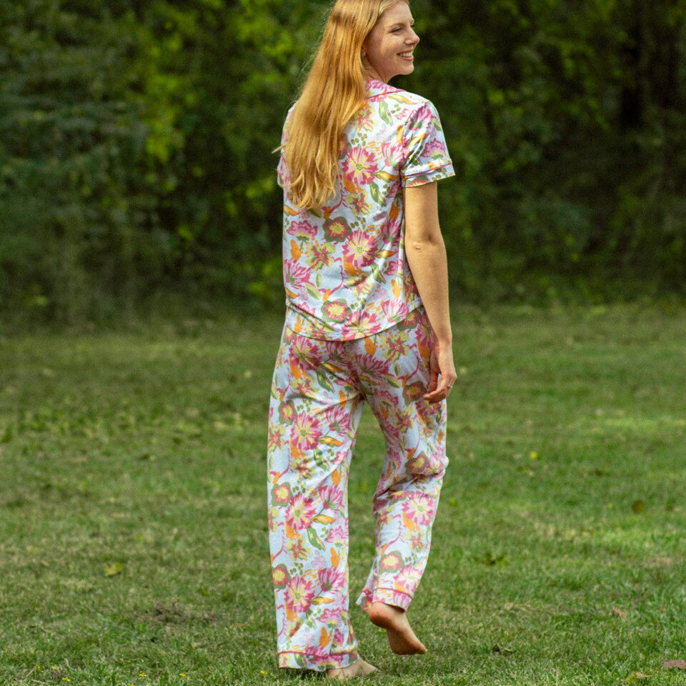 Photograph of a blonde woman standing barefoot in a grassy field wearing a vibrant pink and yellow floral print pajama set