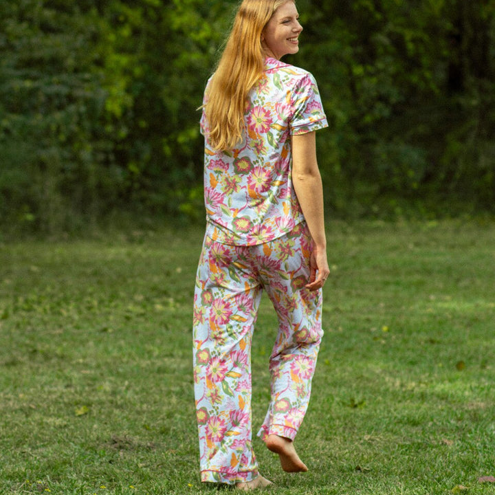 Photograph of a blonde woman standing barefoot in a grassy field wearing a vibrant pink and yellow floral print pajama set