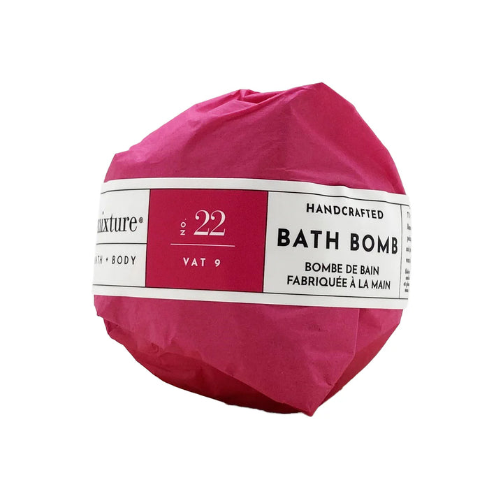 Studio product photograph by Mixture of a handcrafted bath bomb wrapped in vibrant magenta tissue paper featuring a white label with No. 22 and Vat 9 text against a plain white background
