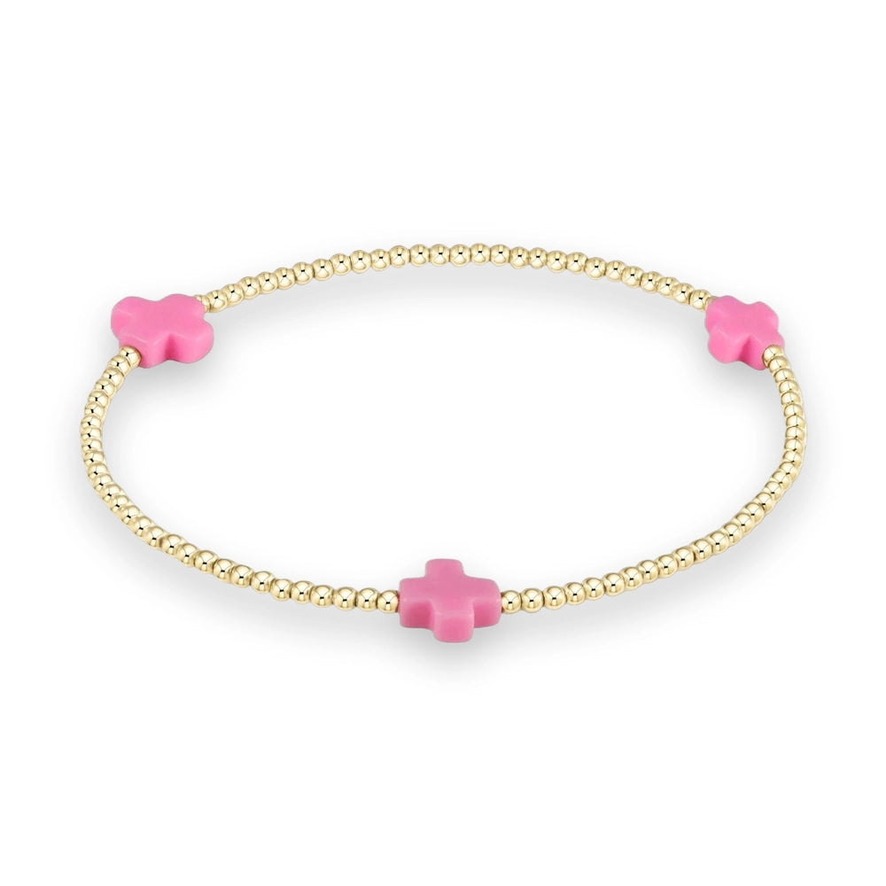 Gold-beaded jewelry bracelet centered on a cream background featuring three matte pink cross charms interspersed with polished gold spherical beads