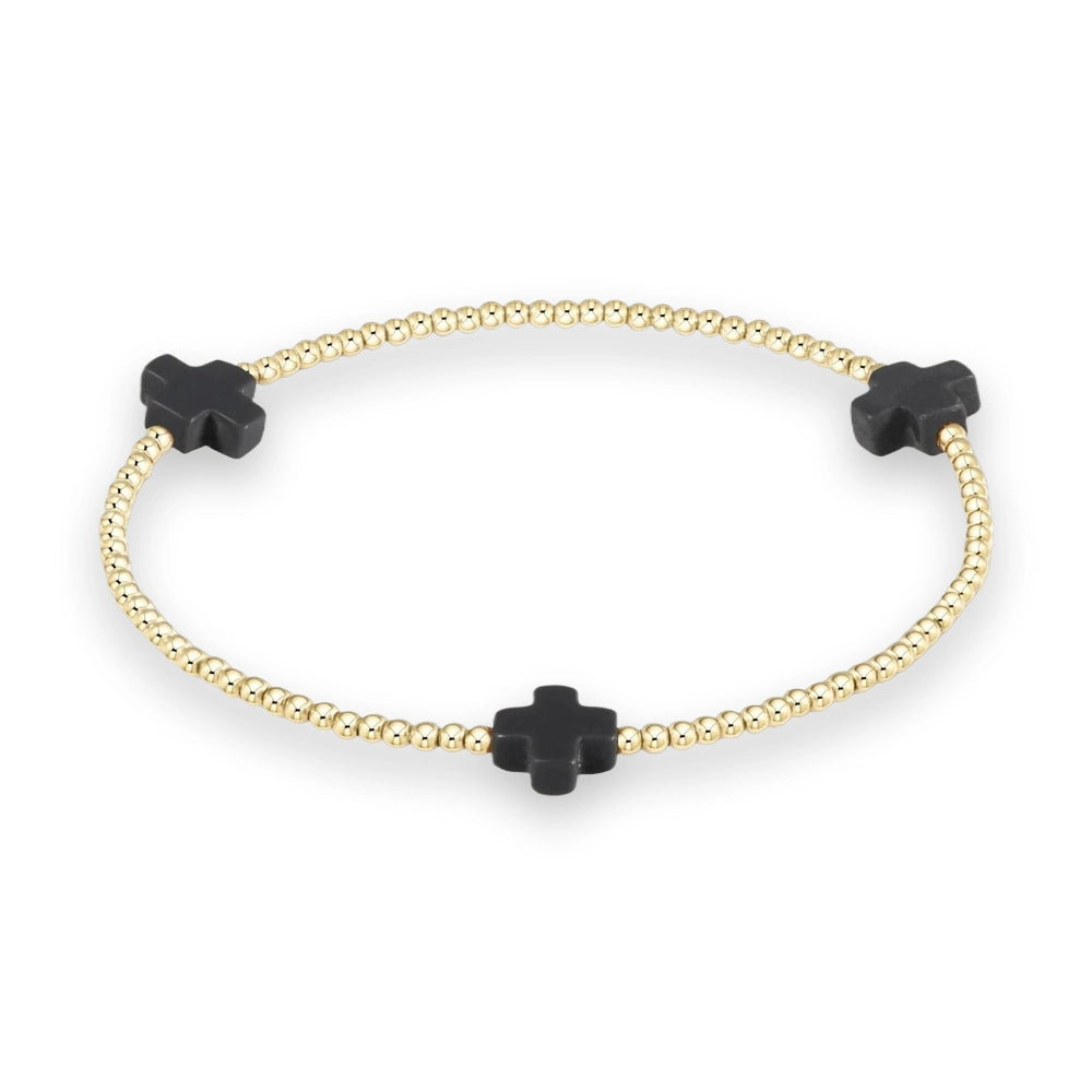 Beaded gold jewelry featuring a circular stretch bracelet composed of small polished spherical beads accented by three equidistant matte black cross charms against a minimalist neutral background
