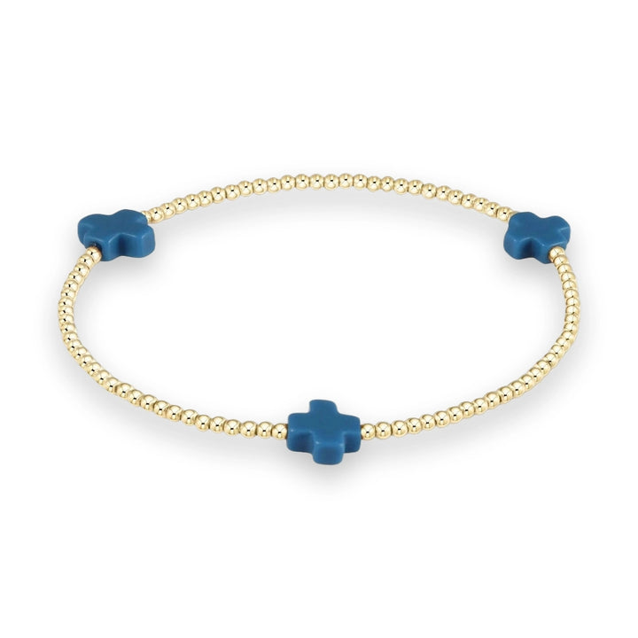 Gold beaded jewelry featuring a minimalist stretch bracelet centered on a neutral background with three matte cerulean blue cross charms and high-polish spherical beads