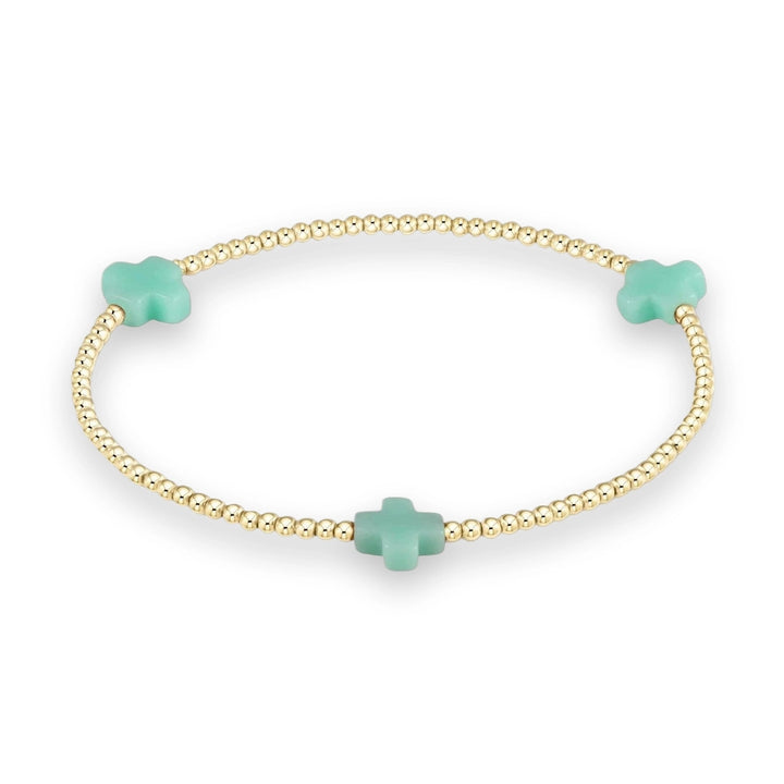 Gold and gemstone beaded bracelet featuring three matte mint green cross charms spaced evenly among polished metallic spheres against a neutral cream studio background