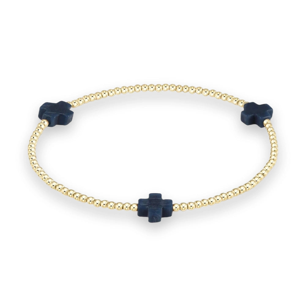 Gold-toned beaded jewelry featuring a circular stretch bracelet on a neutral studio background with three equidistant navy blue cross-shaped stone charms and small polished metallic beads