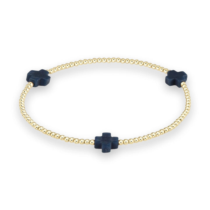 Gold-toned beaded jewelry featuring a circular stretch bracelet on a neutral studio background with three equidistant navy blue cross-shaped stone charms and small polished metallic beads