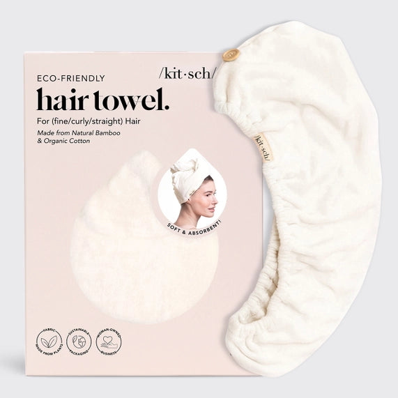 Commercial product photography by Kitsch featuring an eco-friendly hair towel and its pink box packaging, highlighting the plush white bamboo-cotton fabric, a small wooden button, and a circular portrait of a model wearing the towel turban style