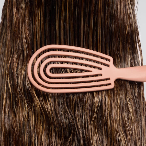 Photograph of a muted rose pink hairbrush with a unique spiral vented head design brushing through thick glossy wet brown hair strands