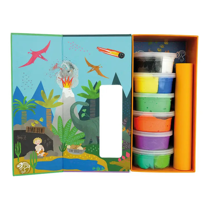 Product photography of a children's dinosaur-themed modeling clay kit featuring an illustrated prehistoric scene with an erupting volcano and a Dino Den cave, alongside stacked tubs of vibrant dough, a flying pink pterodactyl, and a streaking orange meteor