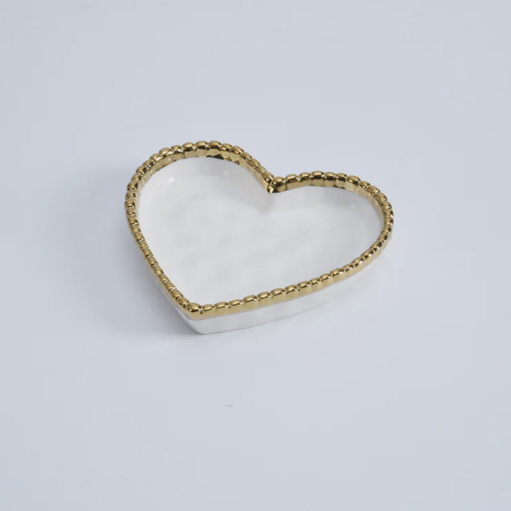 Glazed ceramic heart-shaped trinket dish centered on a minimalist white background featuring a metallic gold beaded rim and a polished white interior