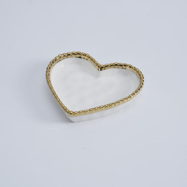Glazed ceramic heart-shaped trinket dish centered on a minimalist white background featuring a metallic gold beaded rim and a polished white interior